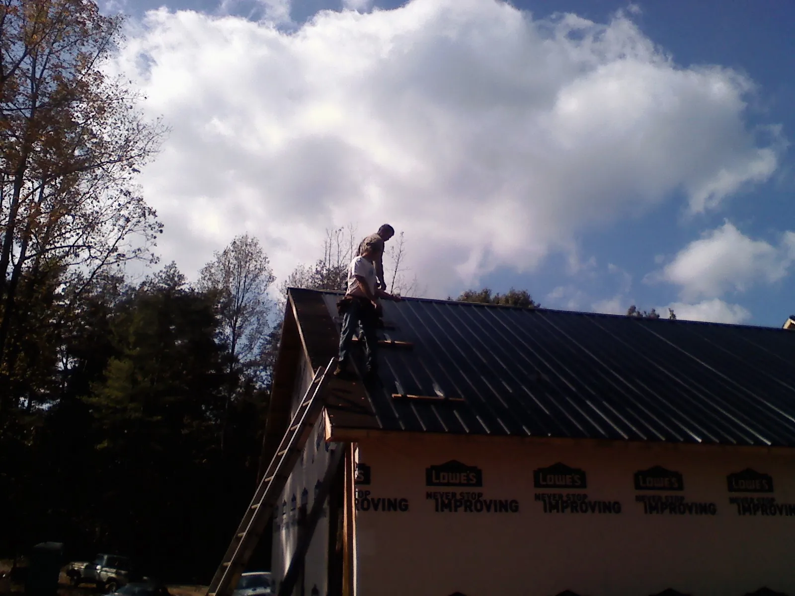 Roofer fastening dark metal panels high against a cloudy sky, from a Roof Inspection job in Willowbrook
